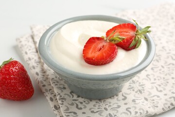 Delicious yogurt in bowl and strawberries on white table, closeup