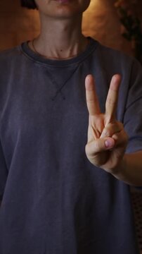 Woman holding two fingers. Casual outfit, wearing t-shirt in a dimly lit room