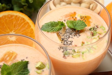 Superfood. Tasty smoothie with chia seeds, mint, pistachio and orange in glasses on white table, closeup