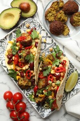 Tasty vegetarian tacos with falafel and other ingredients on white marble table, flat lay