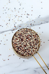 Tri-color quinoa seeds in a measuring cup on white kitchen table. Top view.