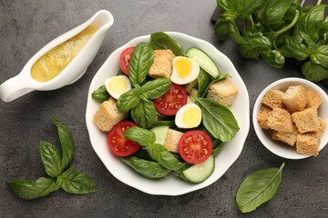Tasty salad with croutons, tomatoes, cucumbers and basil on black table, flat lay