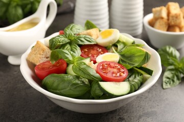 Tasty salad with croutons, tomatoes, cucumbers and basil on black table, closeup