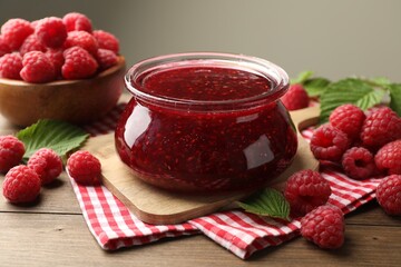 Tasty jam, fresh ripe raspberries and leaves on wooden table, closeup.