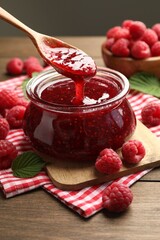 Taking tasty jam with spoon on wooden table, closeup