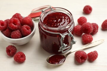 Tasty jam and fresh ripe raspberries on white wooden table, closeup