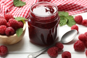 Tasty jam, fresh ripe raspberries and leaves on white wooden table, closeup