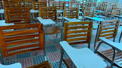 Rows of empty wooden classroom chairs fill the high resolution near windows
