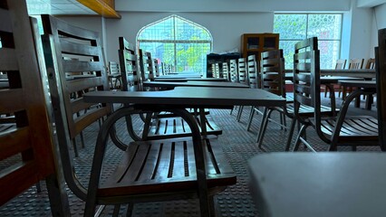 Row of wooden chairs with writing desks face arched windows inside quiet classroom
