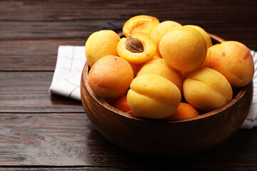 Fresh apricots in bowl on wooden table, closeup