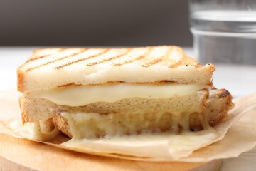 Tasty sandwich with melted cheese and glass of water on table, closeup