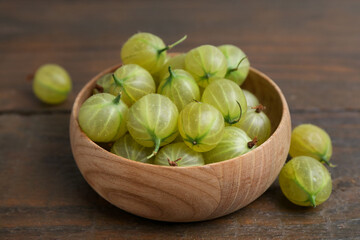 Fresh green gooseberries in bowl on wooden table, closeup