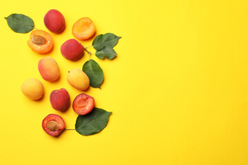 Many fresh apricots and green leaves on yellow background, flat lay. Space for text