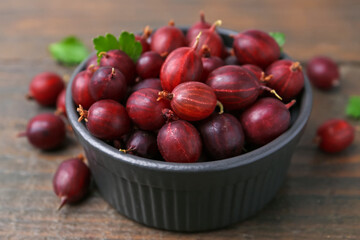 Ripe red gooseberries in bowl on wooden table, closeup