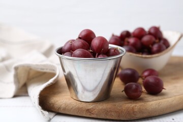 Ripe red gooseberries in bowl on white wooden table, closeup