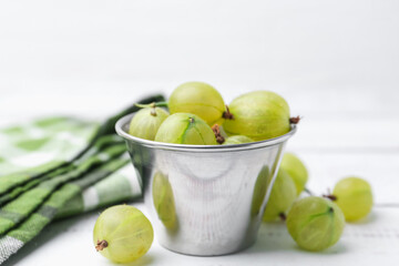 Ripe green gooseberries in bowl on white wooden table, closeup
