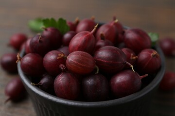 Ripe red gooseberries in bowl on wooden table, closeup
