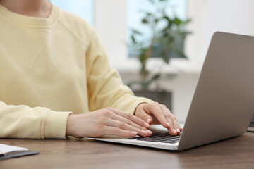 Copywriter using laptop at wooden table indoors, closeup