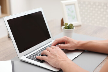 Copywriter using laptop at wooden table indoors, closeup