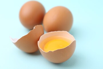 Whole and broken chicken eggs on light blue background, closeup