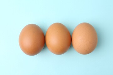 Raw chicken eggs on light blue background, top view