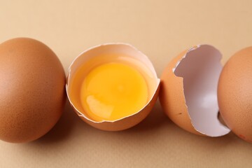 Whole and broken chicken eggs on beige background, closeup