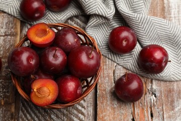 Ripe cherry plums and wicker basket on color wooden table, flat lay