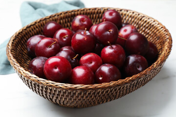 Ripe cherry plums in wicker basket on white table, closeup