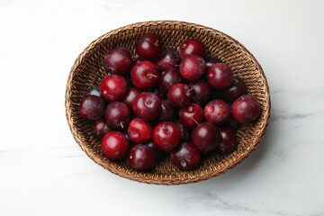 Ripe cherry plums in wicker basket on white marble table, top view