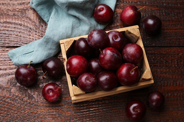 Ripe cherry plums and crate on wooden table, flat lay