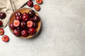 Ripe cherry plums and bowl on grey textured table, flat lay. Space for text