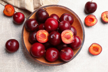 Ripe cherry plums and bowl on grey textured table, flat lay