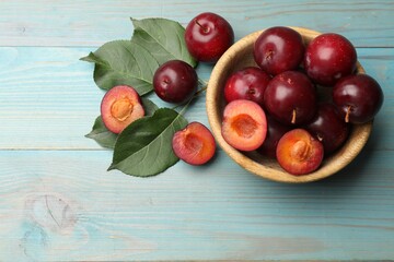 Ripe cherry plums, bowl and green leaves on light blue wooden table, flat lay