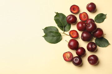 Whole, cut cherry plums and green leaves on light yellow background, flat lay. Space for text