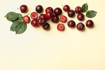 Whole, cut cherry plums and green leaves on light yellow background, flat lay. Space for text