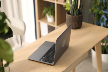 Stylish workplace with laptop on wooden desk and floral decor in office. Biophilic interior design