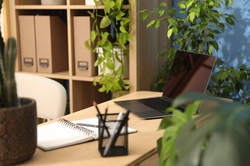 Stylish workplace with laptop, stationery and floral decor in office. Biophilic interior design