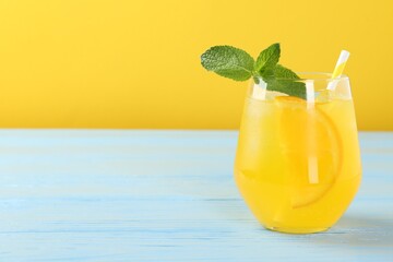 Refreshing soda water with orange slice in glass and mint on light blue wooden table, closeup. Space for text