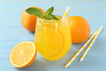 Refreshing soda water with orange slice in glass, mint, fresh fruits and straws on light blue wooden table, closeup
