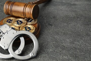 Cryptocurrency. Bitcoins, judge's gavel and handcuffs on grey table, closeup. Space for text