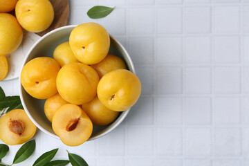 Ripe yellow cherry plums on white tiled table, flat lay. Space for text