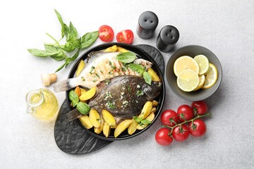 Tasty roasted flounder fish with herbs, potato, lemon slices and tomatoes on light table, flat lay. Homemade seafood dish