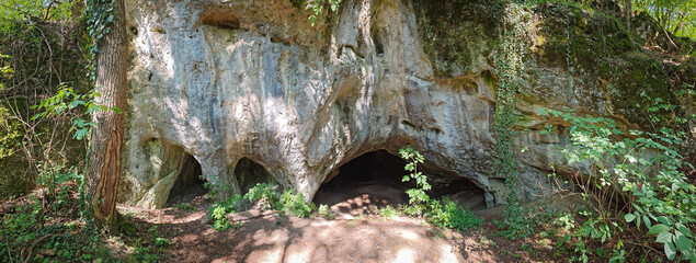 Panoramic view of the multiple entrances of Kő-lyuk Cave, carved into limestone cliffs in the Bükk Mountains, Hungary.