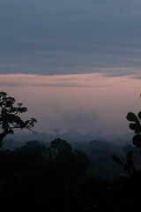 A dreamy and dramatic sunset casting warm light over the fog-covered canopy of the Amazon rainforest