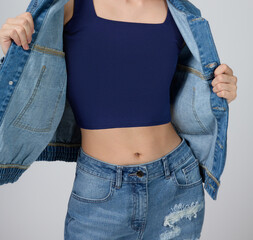Close-up of a young woman wearing a blue crop top and distressed denim jeans, highlighting her fit, sculpted waist. The casual outfit blends comfort, modern style, versatile, healthy lifestyle