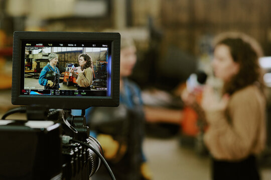 Caucasian middle aged woman and Caucasian young adult woman standing in industrial workshop being filmed by professional camera, monitor displaying both women in conversation - Powered by Adobe