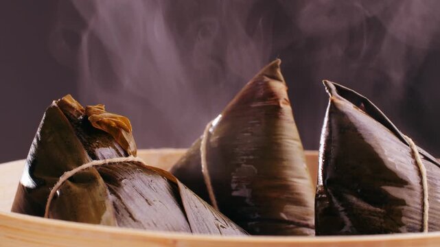 Hand holding zongzi (rice dumpling) with savoury fillings wrapped in bamboo or reed leaves.