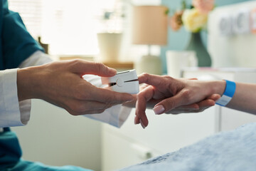 Caucasian middle aged woman lying in hospital bed receiving care from medical professional, nurse placing pulse oximeter on patient finger, healthcare setting visible in background