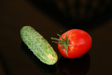 Harvest of cucumbers and tomatoes on a black mirror background.