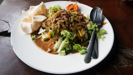 Indonesian specialty food, namely gado-gado, which is served on a white plate on a wooden table